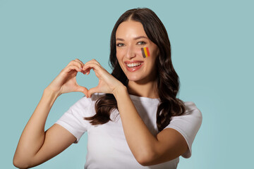 Happy lady forming heart shape with her hands, showing love to Romania, posing with flag painted on...