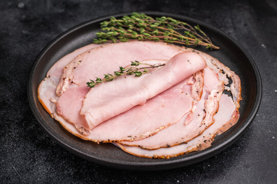 Charcuterie style cured pork lonza on a black plate with herbs against a moody textured background ideal for culinary photography and stock images.