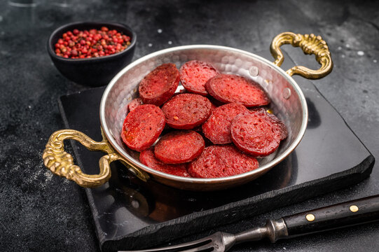 Fried Turkish sucuk (sujuk) in a copper pan on a dark stone background with copy space. Traditional breakfast.
