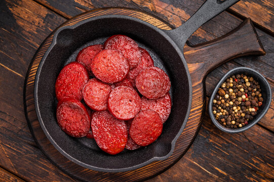 Fried Turkish sucuk (sujuk) slices in a cast iron pan with thyme and spices on a dark rustic wooden table.