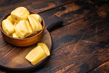 Sweet, golden jackfruit pods (bulbs) in a wooden bowl on a rustic dark wood table. Tropical fruit snack with copy space. © Mironov