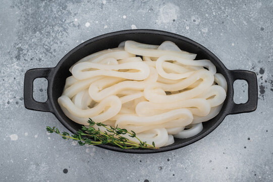 Fresh calamari rings in cast iron bowl with thyme on textured gray background ideal seafood ingredient for gourmet cooking.