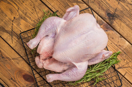 Whole fresh raw chicken on a cooling rack with rosemary and thyme. Ready for cooking on a rustic wooden table.