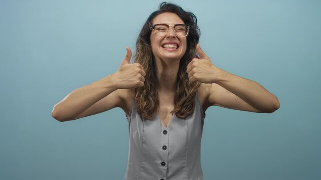 Eager woman displaying thumbs up gesture with hand and big wide grin in vibrant blue studio; approval.