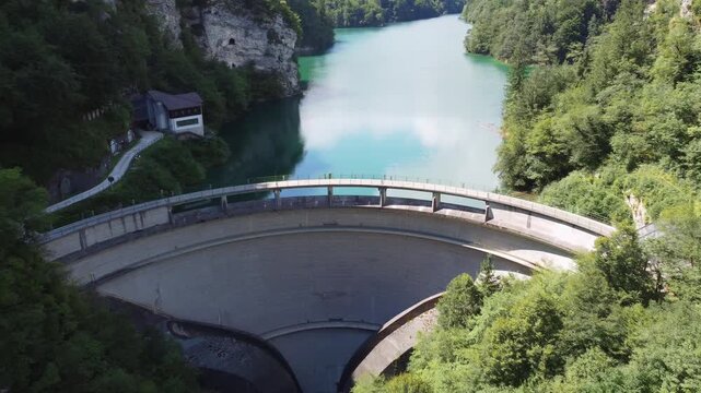 Aerial drone view of the Senaiga dam and the turquoise artificial Lake Senaiga surrounded by lush forest, steep rock walls, and mountain scenery in summer in Lamon, Belluno, Veneto, Italy