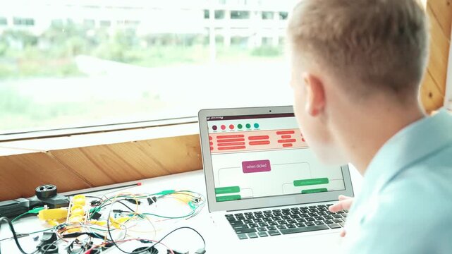 Caucasian student looking at laptop screen while coding engineering prompt or programming system. Back view of teenager working by using computer and electronic tool repair main board.. Edification