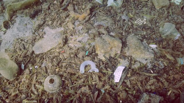 Panorama rock-sand seabed covered with plastic trash and oter debris, Closeup, Slow motion. Concept plastic pollution of Ocean 