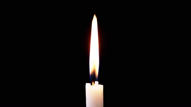 Isolated burning candle with bright flame on dark background. One white wax candle with calm yellow flame illuminates on black background. Copy space. Slow motion. Concept of memory, celebration.