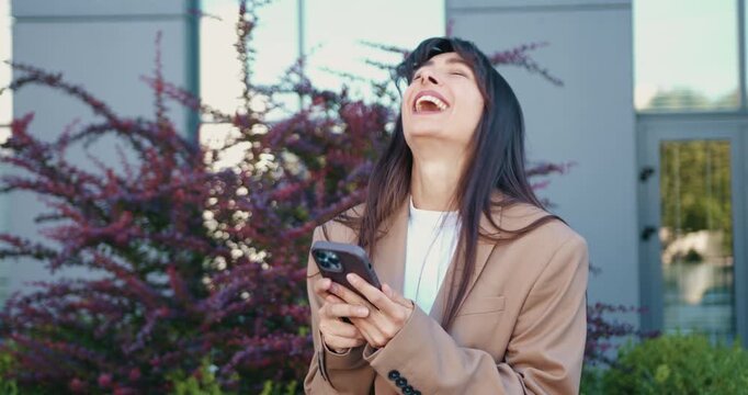 Surprised Caucasian woman using smartphone outdoors in urban park, reacting to good news while looking at screen. Emotions and communication concept.