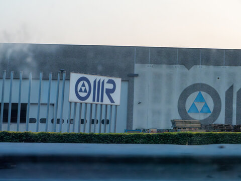 Exterior view of a modern industrial facility featuring the OMR company logo and a large blue triangular symbol on its facade