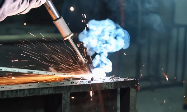 Worker guides welding tool over rusted metal in gritty workshop setting
