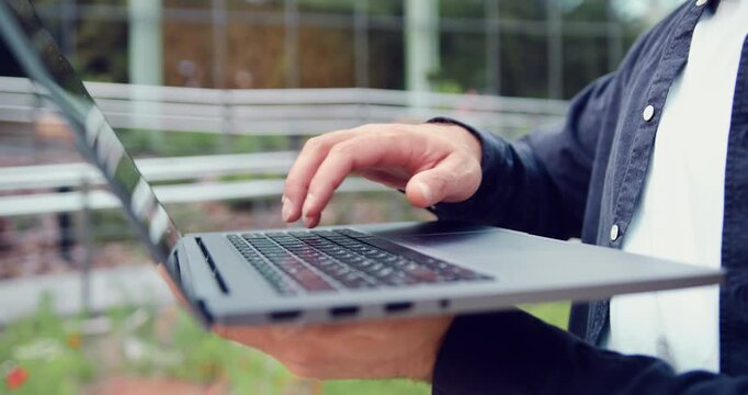 Close-up side view of a man hand interacting with a laptop outdoors, tapping and scrolling, representing digital communication and computers technology in everyday life