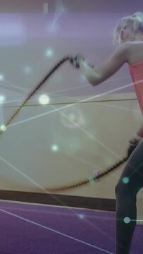 Vertical video: Holding ropes, woman doing alternating waves for fitness, particles accenting ropes