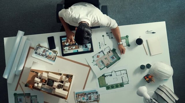 Top view of business man using tablet plan house design while sitting at meeting table with blueprint and equipment scatter around. Aerial view of civil engineer working at blueprint. Alimentation.