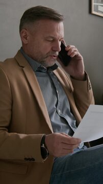Verical shot of middle aged man speaking urgently on his phone, while waiting in queue in modern bank office