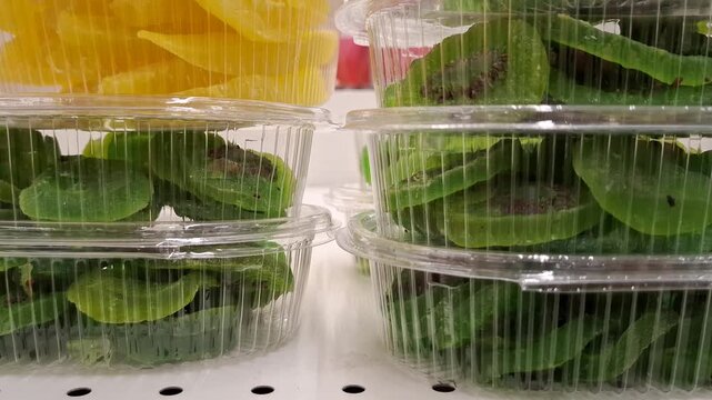 Transparent plastic containers filled with green dried kiwi slices and yellow mango pieces on a store shelf. Colorful dried fruits, healthy snacks, natural organic food