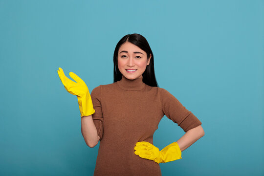 Pleased cheerful and positive asian houseworker from chores wearing yellow rubber gloves pointed her hand at copy space, Cleaning home concept, Smiling happy and optimistic housekeeper