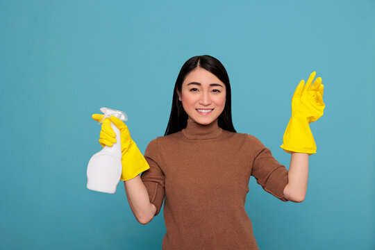 Delighted smiling and optimistic asian houseworker at work holding spray in yellow rubber glove isolated on a blue background, Cleaning home concept, Laughing joyful female from day to chores