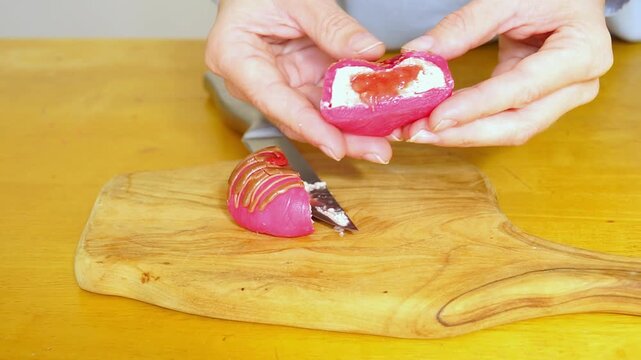 Hands pressing strawberry mochi half with a creamy interior and berry center. Captures tactile food response, compression texture effect, visual satisfaction trigger, and interactive dessert moment.