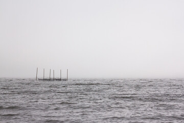 Minimalist foggy landscape of Lake Paravani with traditional wooden fishing nets in the water, Georgia. © Ewa Bogucka