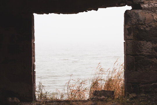 Framed view of the misty Paravani Lake through an old ruined stone window with dry grass, Georgia.