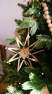 Natural straw star ornament hangs on a green Christmas tree with soft lights