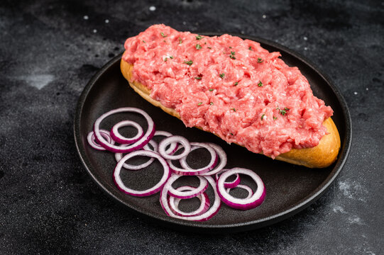 Raw beef cannibal sandwich with minced beef and red onion served on bread roll on black plate