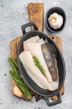 Fresh dab flatfish fillets with herbs and garlic in cast iron pan, raw seafood ingredient for healthy cooking on light textured background