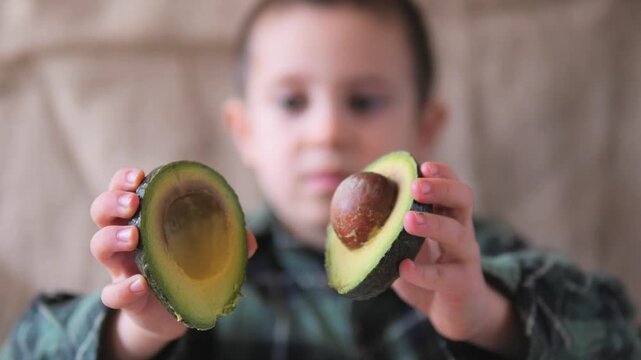 Boy Holding Two Halves of Avocado Toward Camera &mdash; Child Presenting Fresh Avocado with and without Pit, Healthy Food Concept, Kids Nutrition Lifestyle