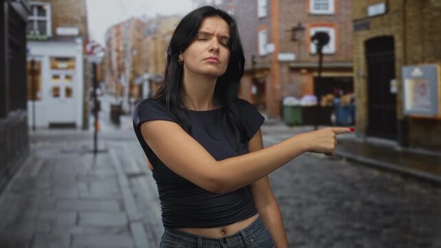 Woman pointing finger forward on street with furrowed brow and tense posture under soft daylight; rejection.