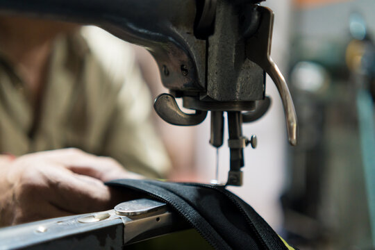 Latino upholsterer meticulously repairs a backpack using a vintage sewing machine in his workshop