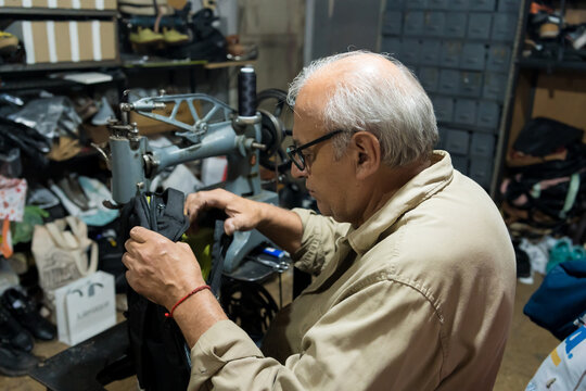 Latino upholsterer meticulously repairs a backpack using a vintage sewing machine in his workshop