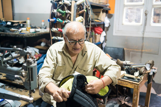 Experienced Latino upholsterer meticulously repairs a backpack in his cluttered workshop