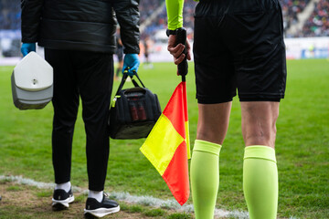 Fototapeta premium Close-up of an assistant referee holding a yellow-red flag beside a medical staff member at a professional soccer stadium sideline.