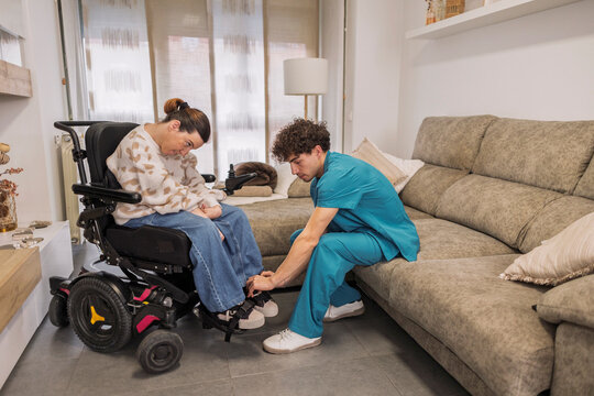 Caregiver assisting woman in electric wheelchair at home