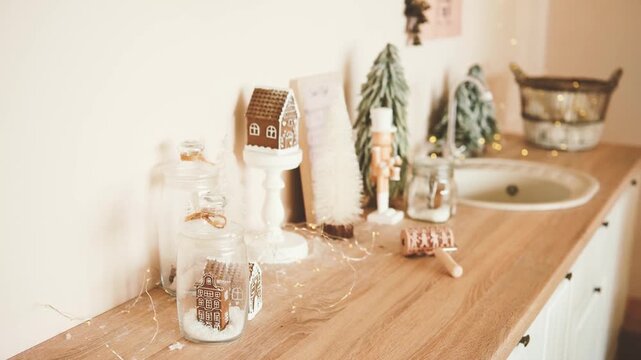 Cozy Christmas decorations with gingerbread house, trees, nutcracker and fairy lights on a wooden counter.