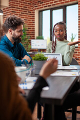 Black entrepreneur using tablet to outline company plans to colleagues during discussion in modern...
