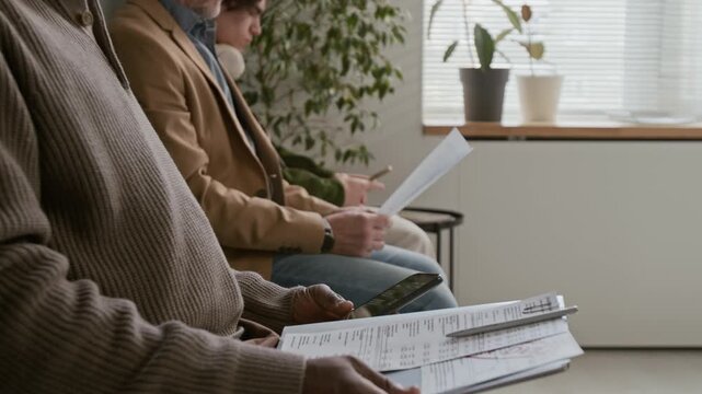 Handheld zoom out shot of three unrecognizable men in smart casual outfits waiting with documents in bank