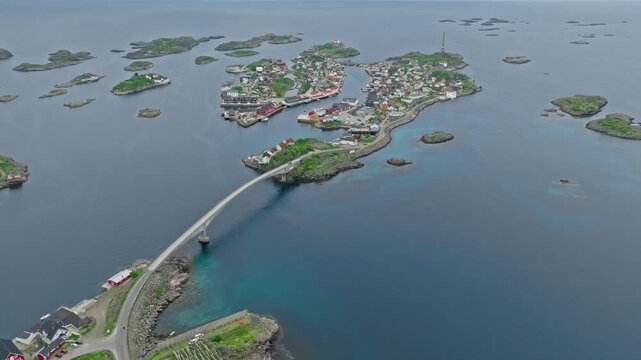 Aerial drone approaching Henningsv&aelig;r village from the sea with bridge access and colourful houses on small islands. Picturesque coastal settlement in the Lofoten Islands.