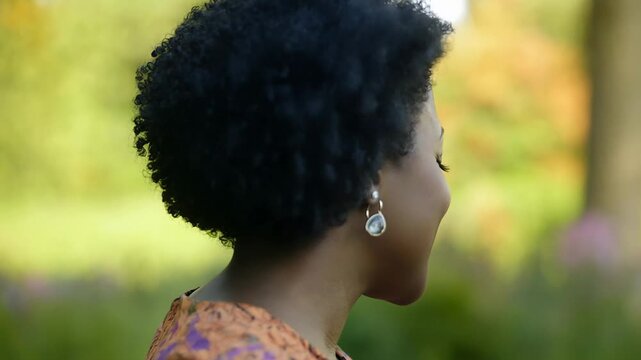 Close-up profile of a smiling Black woman with natural hair and earrings outdoors
