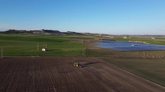 Aerial Rural Landscape with Tractor Working Field, Solar Panels and Sheep Near Small Village