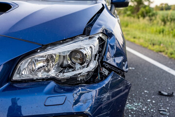 Blue car with shattered headlight and crumpled fender on roadside