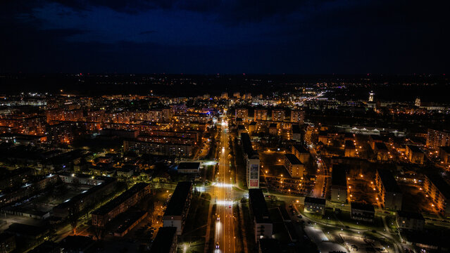 Aerial drone footage of a small provincial town in Poland at night, glowing street lights, quiet urban landscape, peaceful atmosphere, and illuminated roads under dark sky.