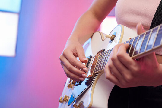 Woman hands playing an electric guitar on stage with colorful pink and blue lights