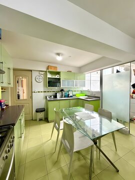A modern, bright kitchen with a glass-enclosed dining area and green accents