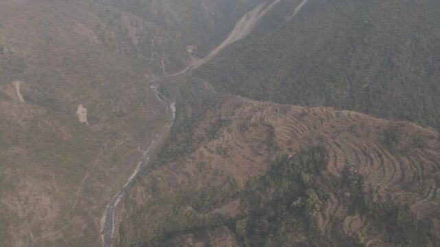 Top-down aerial view of Sainji corn village near Mussoorie, Uttarakhand, with terrace farms and houses forming abstract patterns on misty slopes, with the Aglar River flowing below.