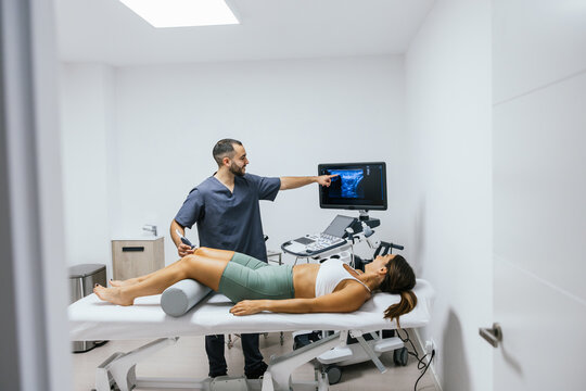 Physiotherapist performing an ultrasound scan on a female patient's knee in a clean clinic, identifying musculoskeletal issues for diagnosis