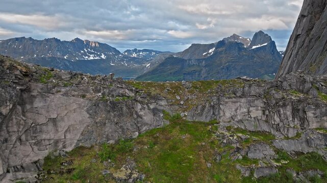 Drone aerial overlooking fjord and mountains near Segla on Senja Island, Norway. Scenic Arctic landscape with steep ridges and calm reflective waters.