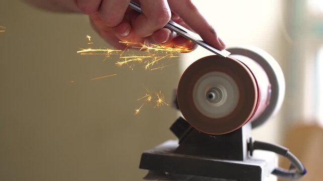 Sharpening Metal Tool on Grinding Wheel with Bright Flying Sparks in Workshop
