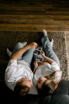 A couple sits on a rug looking at ultrasound photos. The mood is intimate and joyful as they anticipate parenthood. Perfect for family planning or pregnancy blog content.